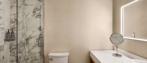 A modern bathroom with a glass shower enclosure, a toilet, a sink with a marble countertop, and a mirror.