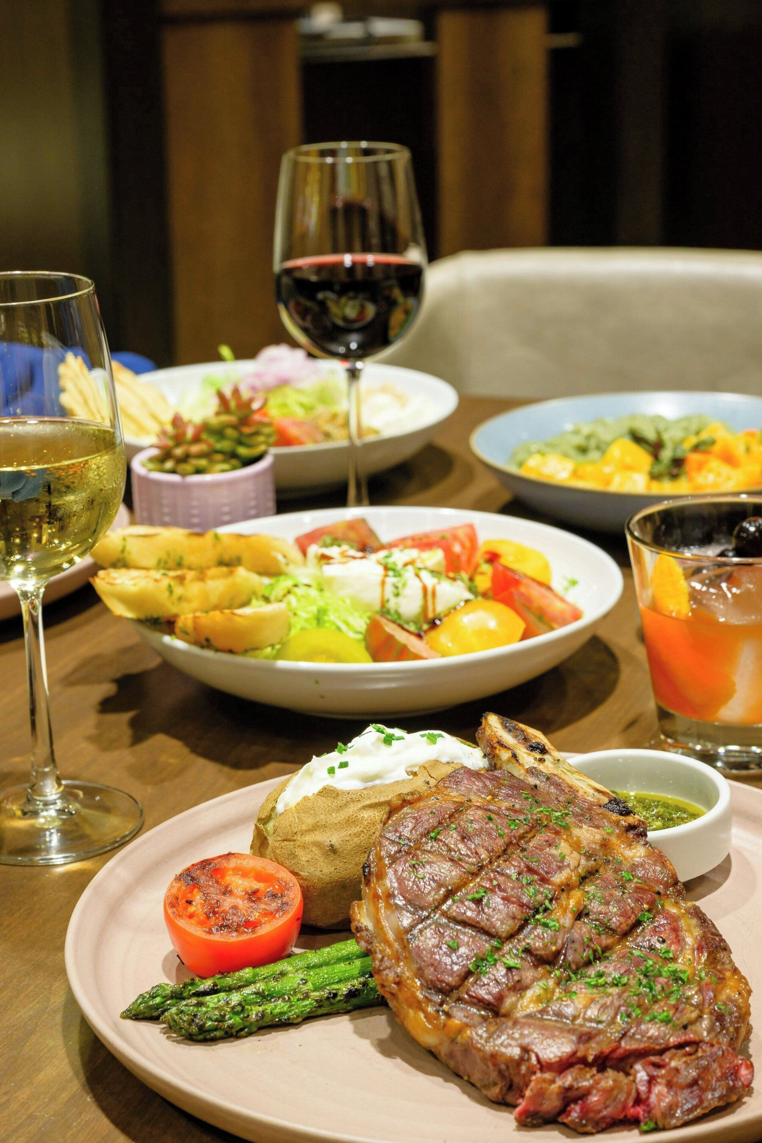 Una mesa de comedor con una variedad de platos, incluyendo carne, verduras y una copa de vino tinto.