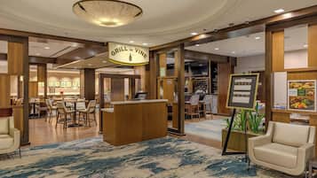 A hotel lobby with a central reception desk, multiple seating areas, and a bar.
