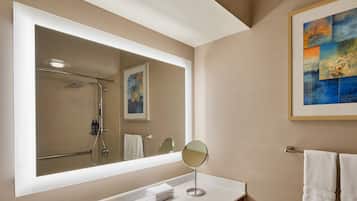 A modern bathroom with a large mirror, a white sink, and a framed abstract painting on the wall.