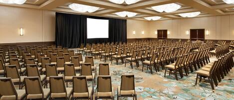 A conference room with rows of chairs, a large screen, and a stage with curtains.
