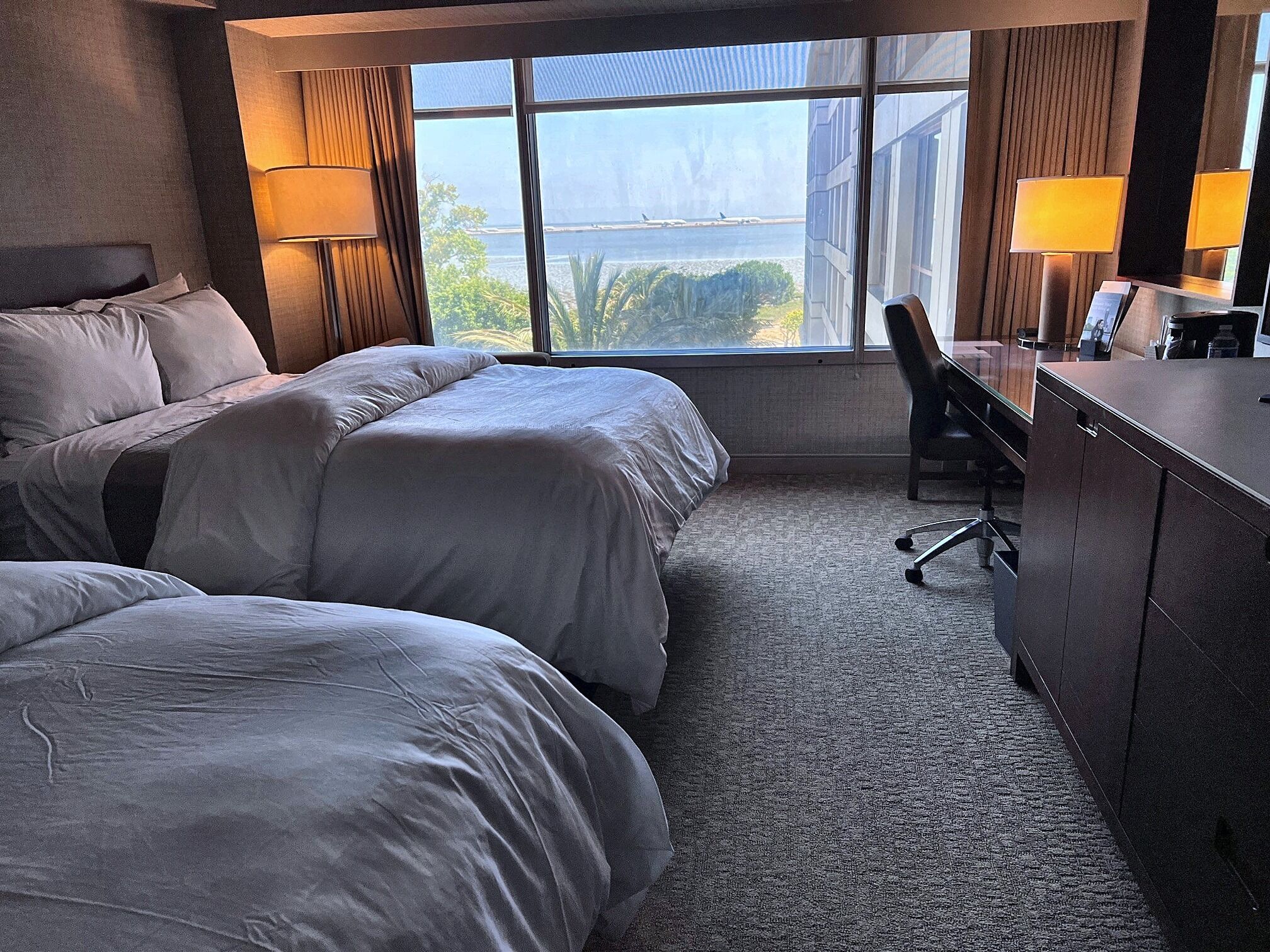 A hotel room with two beds, a desk, and a view of a body of water.