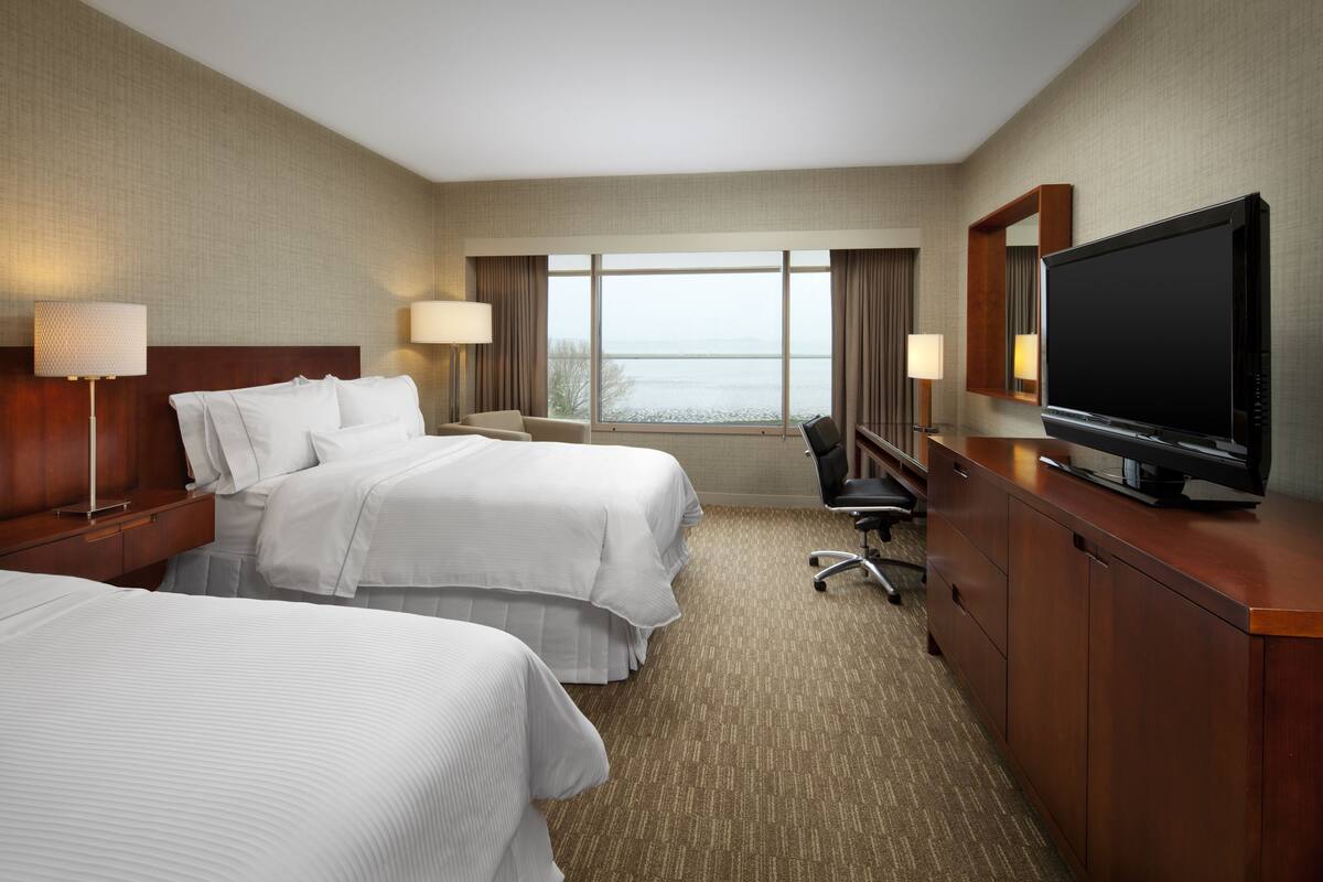 Une chambre d’hôtel avec deux lits, un bureau, une télévision et une vue sur l’eau.