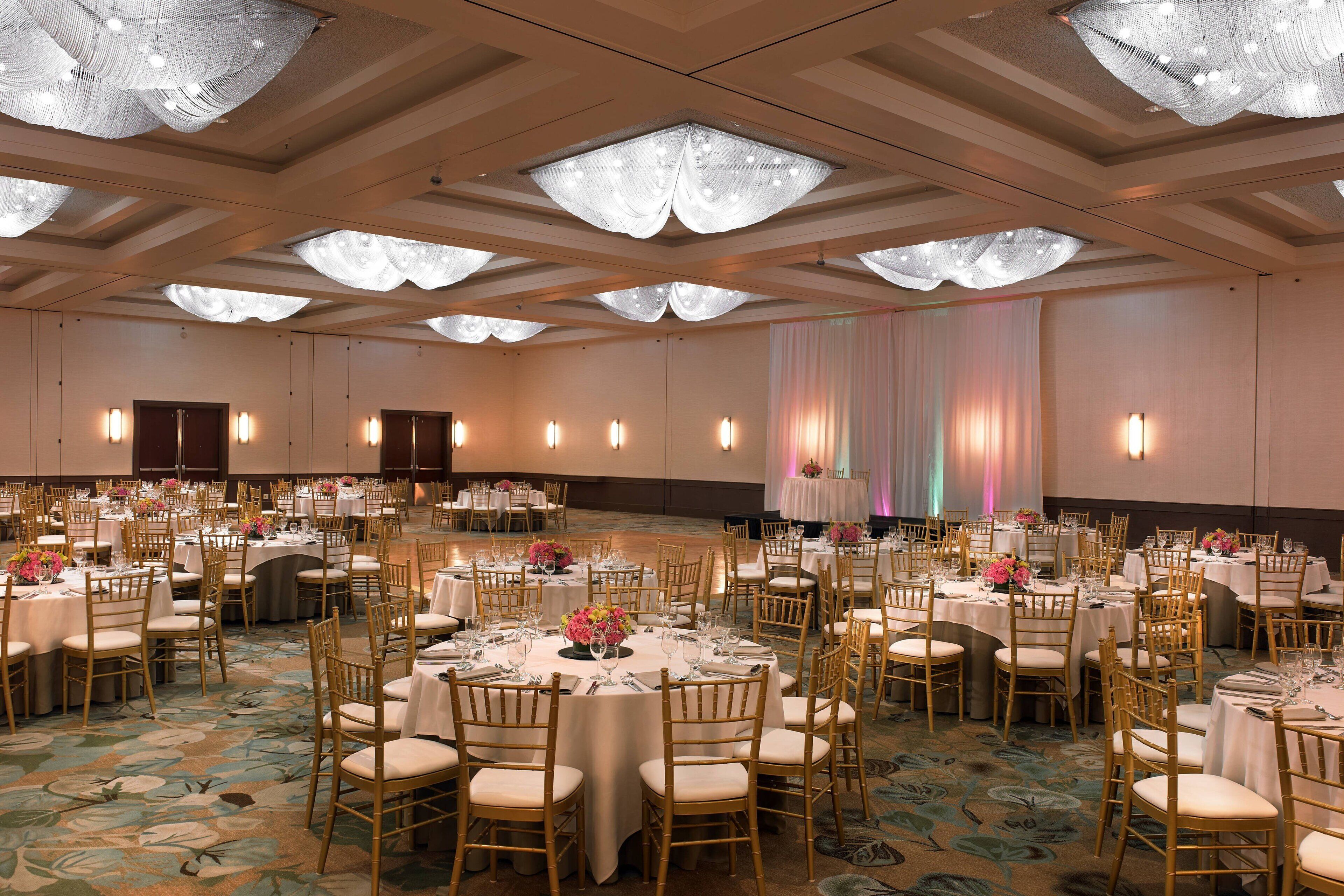 A banquet hall with round tables, chairs, and floral centerpieces.