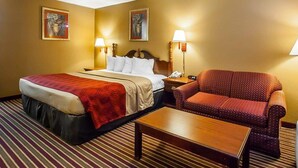 A hotel room with a bed, a chair, a table, and two wall-mounted lamps. - Econo Lodge Dyersburg I-155 (Dyersburg)