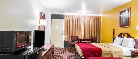 Una habitación de hotel con una cama, un escritorio con computadora, televisor y una puerta.