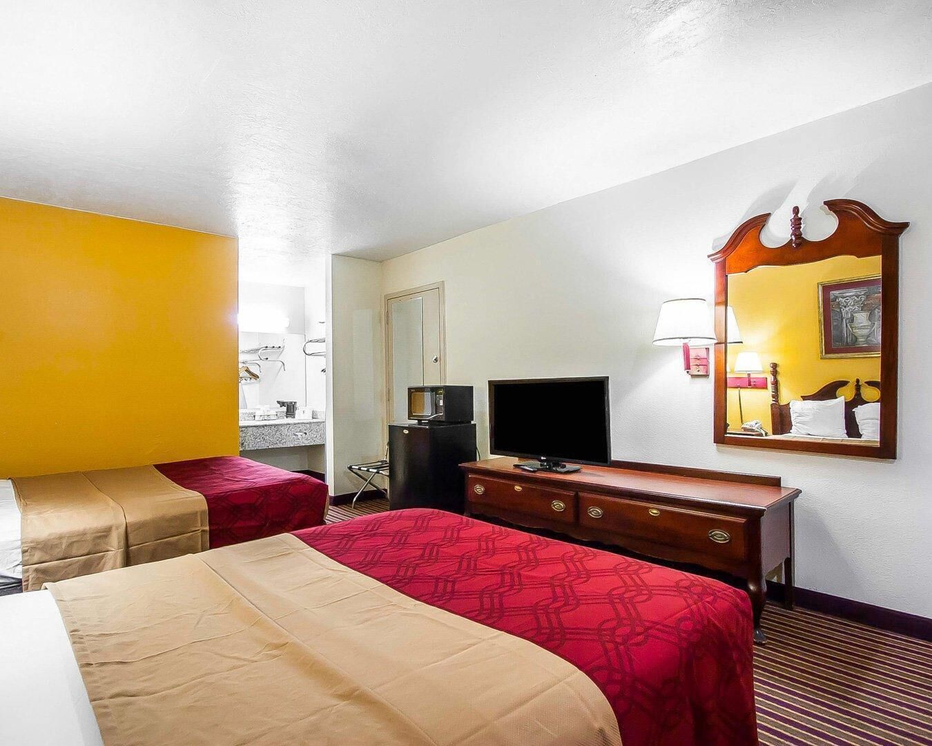 Una habitación de hotel con dos camas, televisión, cómoda y espejo.