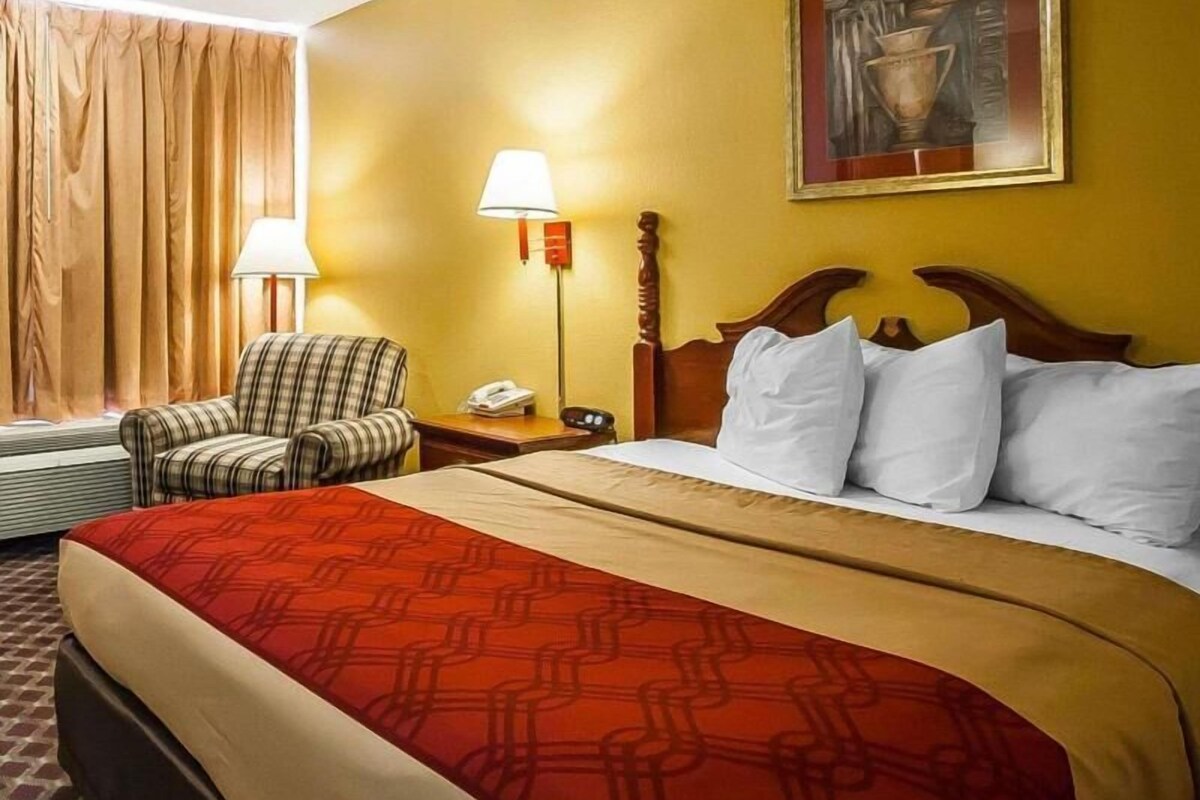 A hotel room with a bed, a chair, a nightstand, a lamp, and a painting on the wall.