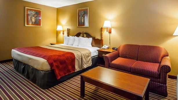 A hotel room with a bed, a chair, a nightstand, and two wall-mounted lamps. - Econo Lodge Dyersburg I-155 (Dyersburg)