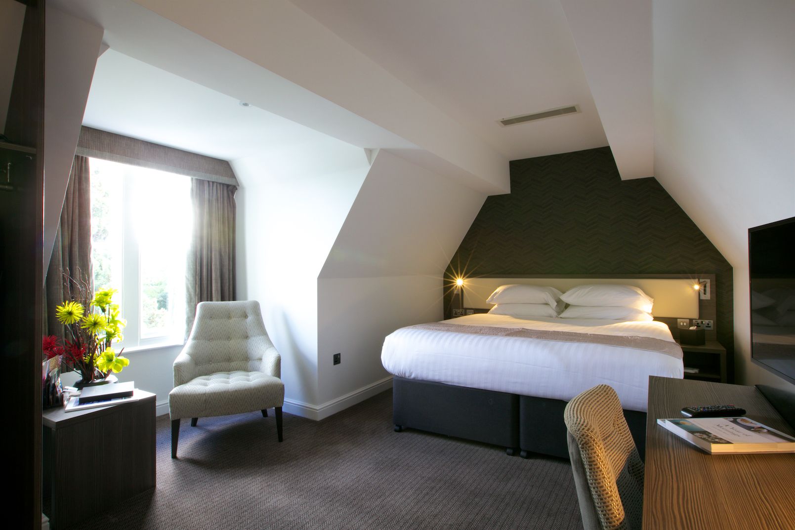 Una habitación de hotel con cama, una silla, un escritorio y una televisión.