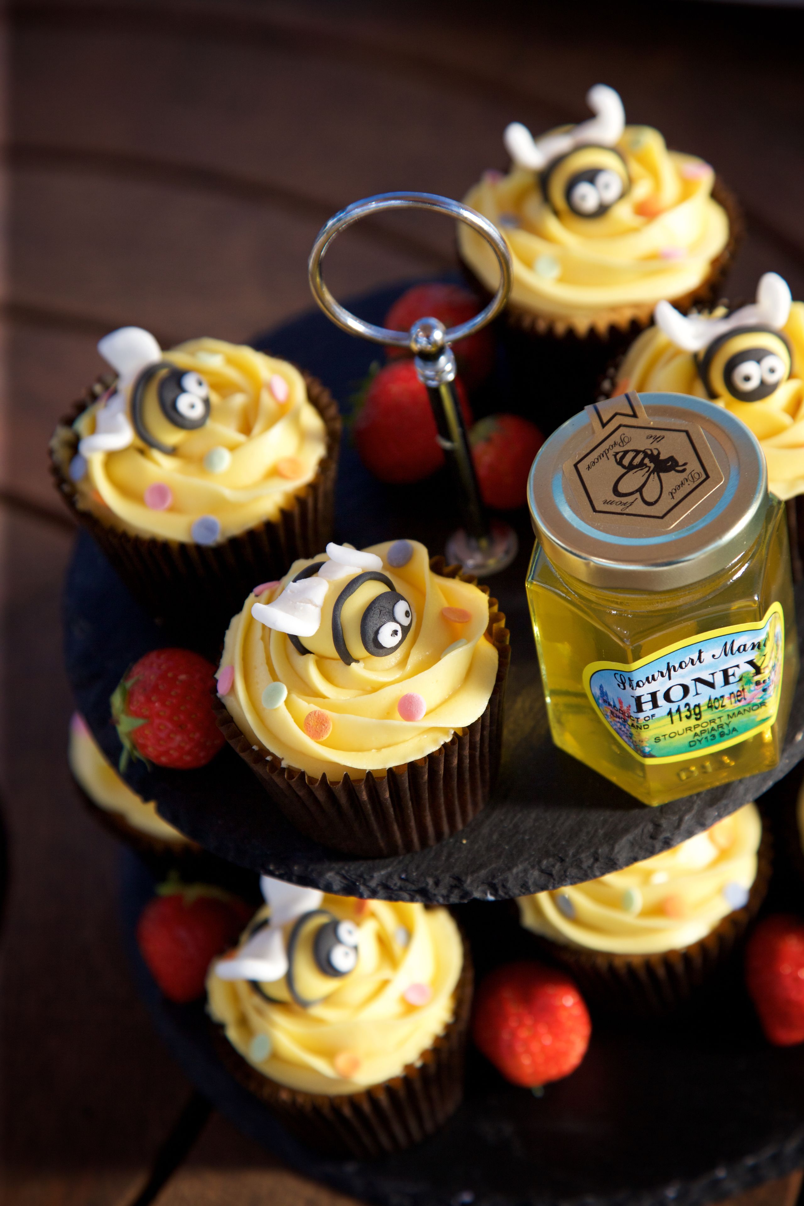 A tiered stand with cupcakes and a honey jar.