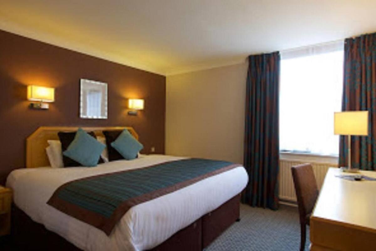 Ein Hotelzimmer mit Bett, Nachttischlampen, Schreibtisch und einem Fenster mit Vorhängen.