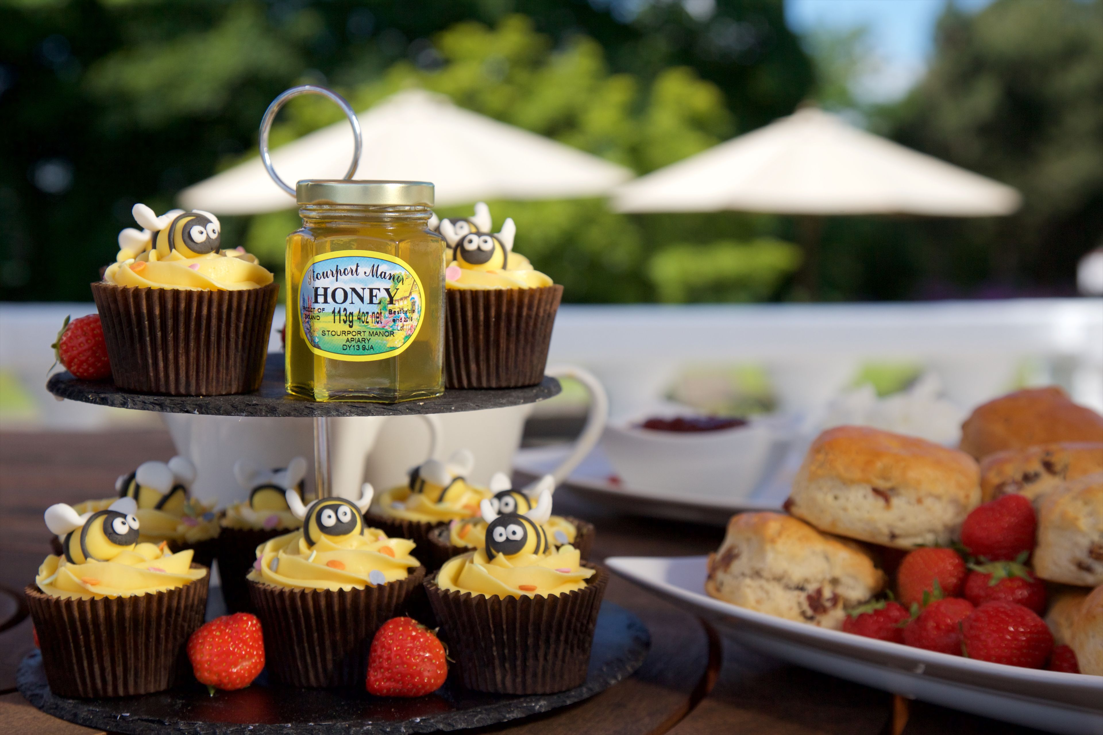 A dessert table with cupcakes, a honey jar, strawberries, and scones.