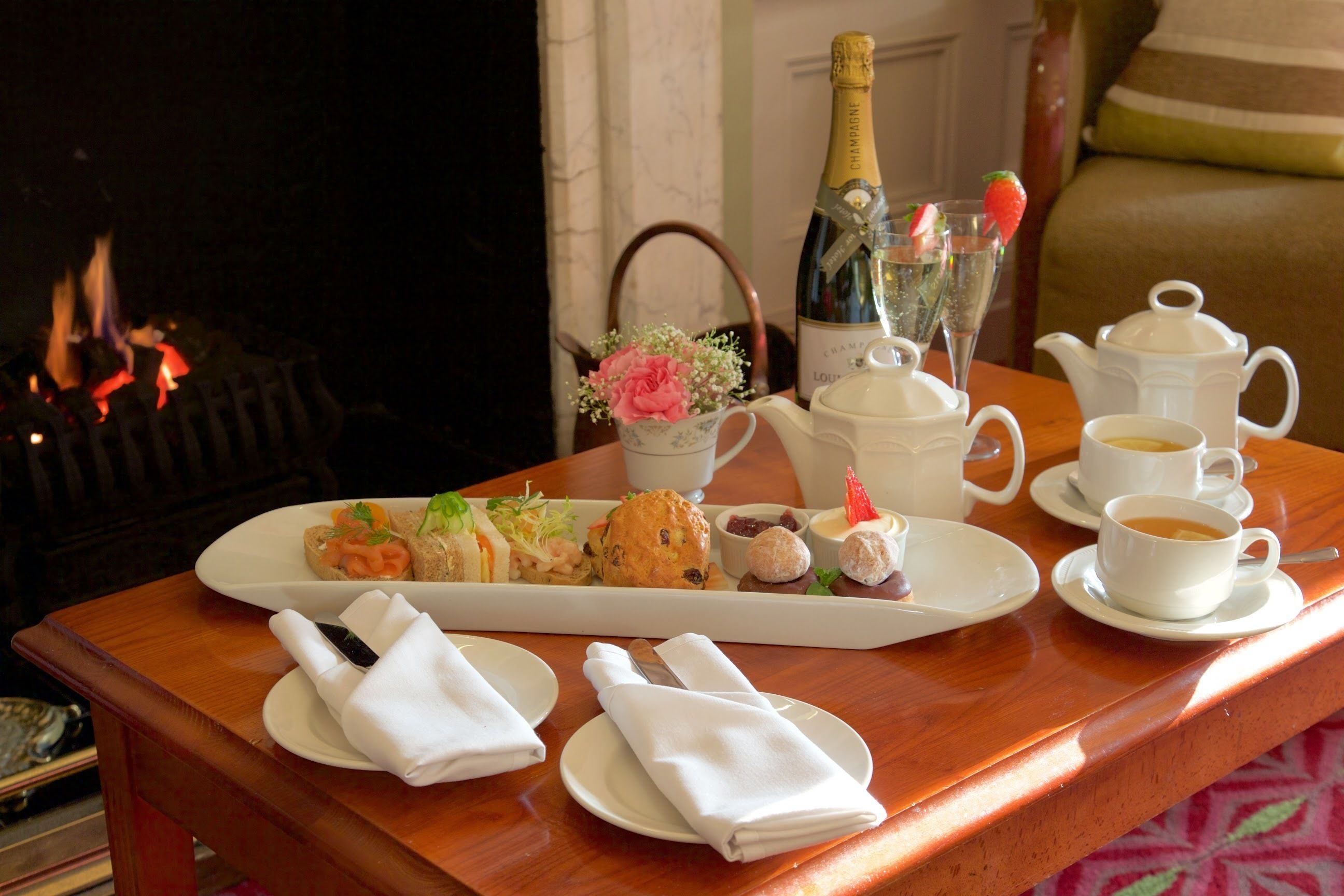 A breakfast setup with a variety of pastries, a bottle of champagne, and coffee cups on a wooden table.