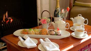 A breakfast setup with a variety of pastries, a bottle of champagne, and coffee cups on a wooden table.