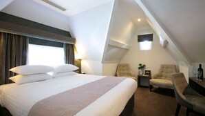 Habitación de hotel con una cama grande, dos sillones, una mesita y una ventana con cortinas.
