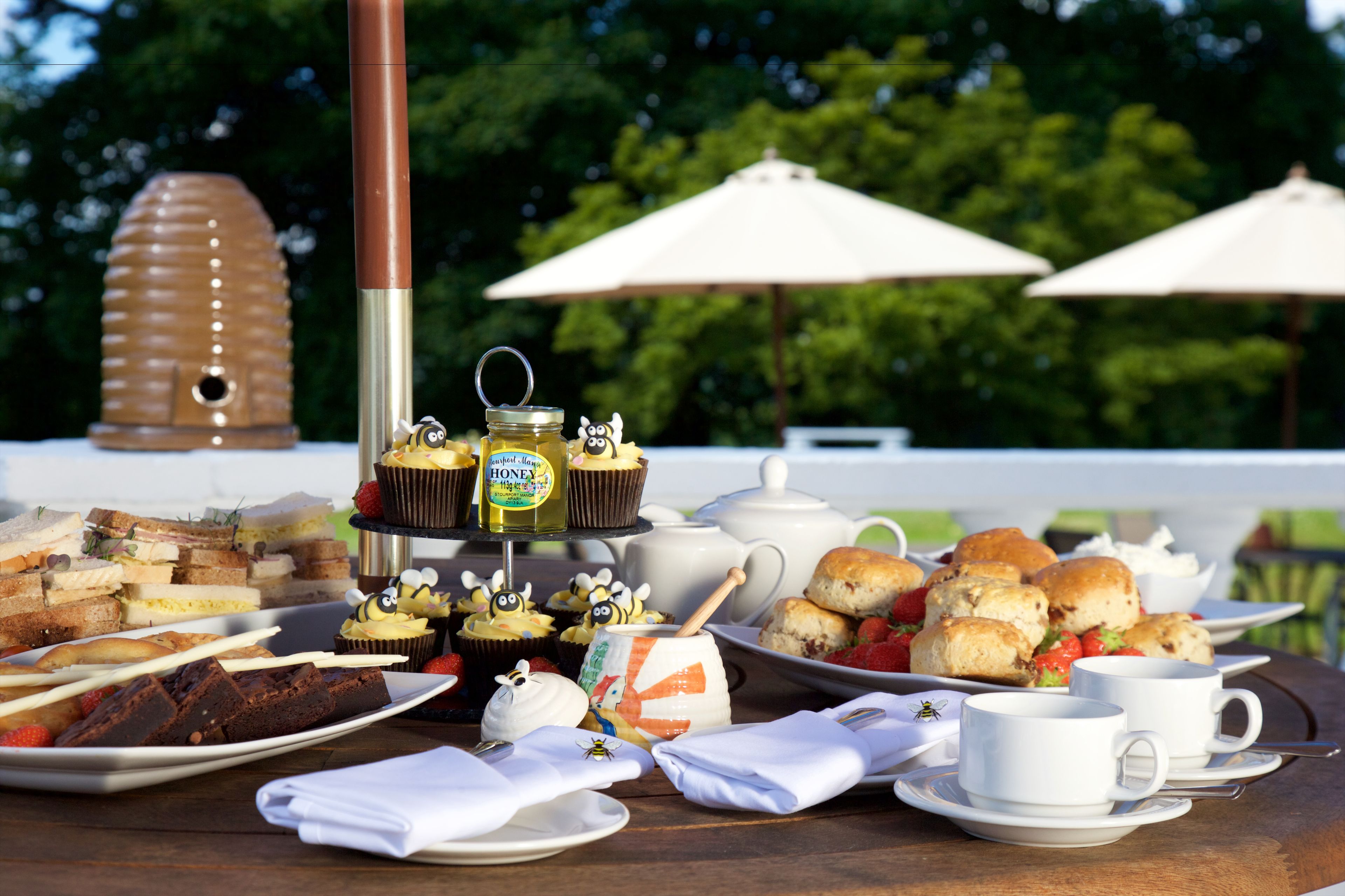 Une table dressée avec divers aliments, notamment des sandwichs, des scones et des cupcakes, ainsi qu’une théière et des tasses.