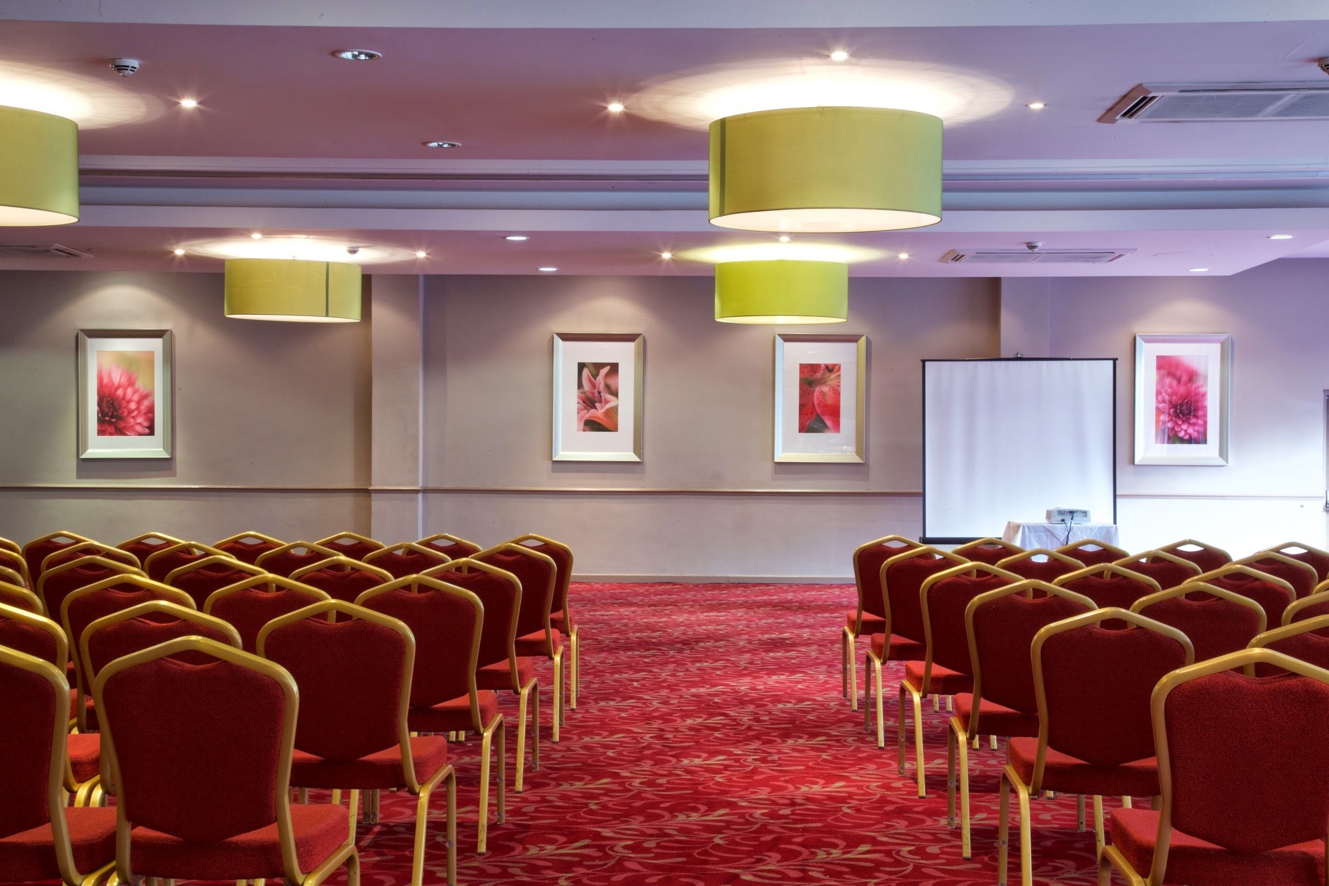 A conference room with rows of red chairs and a projector screen on the wall.