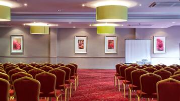 A conference room with rows of red chairs and a projector screen on the wall.