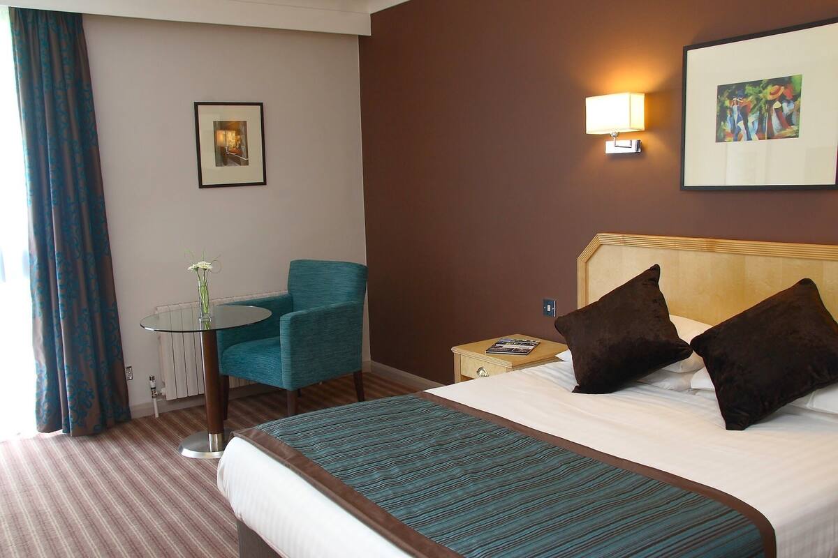 Ein Hotelzimmer mit Bett, Stuhl, Tisch und einem Bild an der Wand.