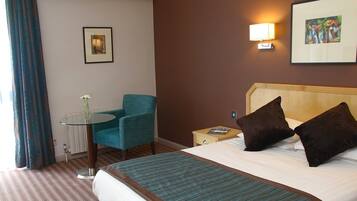 Una habitación de hotel con una cama, una silla, una mesa y un cuadro en la pared.