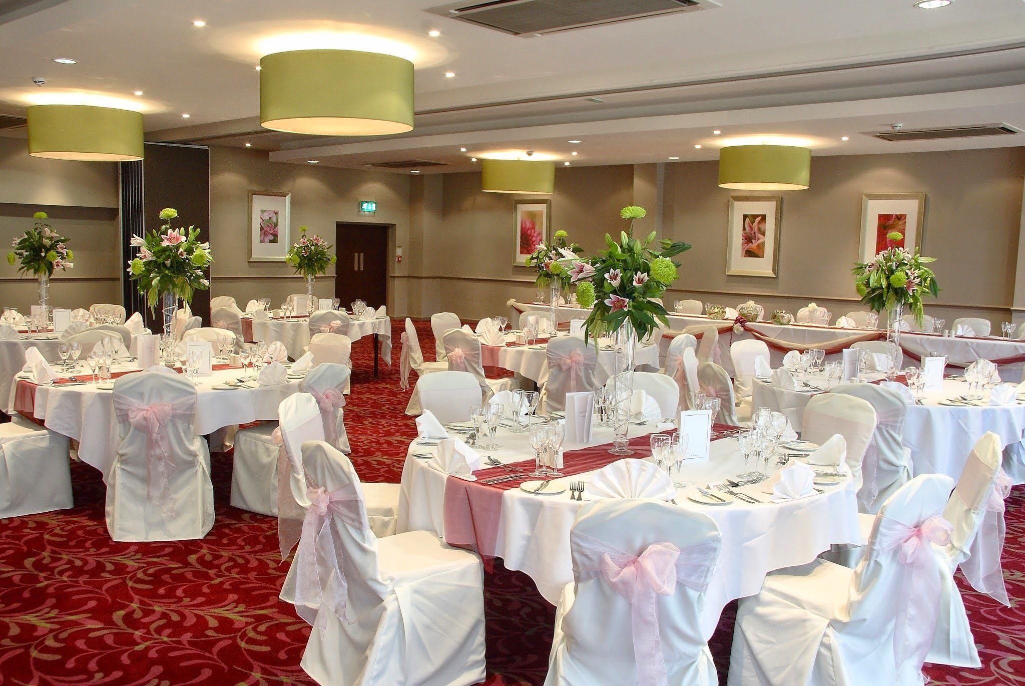 Un salón de banquetes con mesas redondas, sillas blancas y centros de mesa florales.