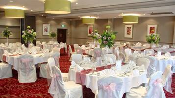 Un salón de banquetes con mesas redondas, sillas blancas y centros de mesa florales.