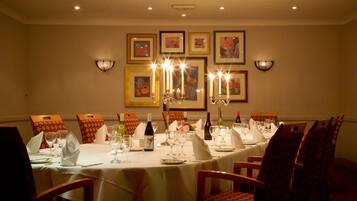 A dining room with a long table set for a meal, framed artwork on the walls, and wall-mounted lighting.