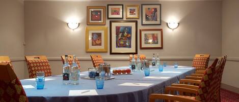 A conference room with a long table, chairs, framed artwork on the wall, and table settings including water bottles and glasses.