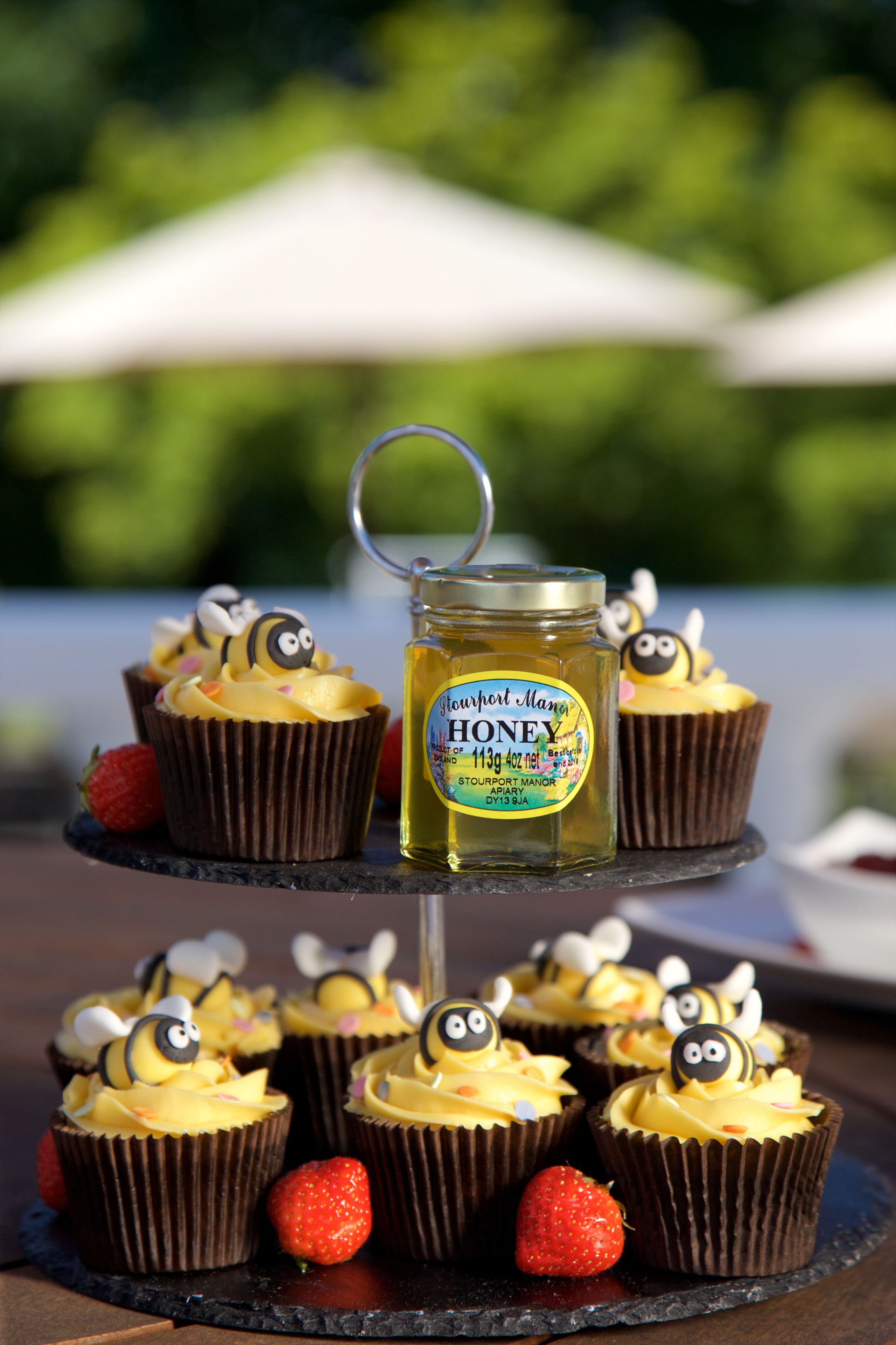 A tiered stand with cupcakes topped with bee decorations and a jar labeled "Stourport Manor Honey."