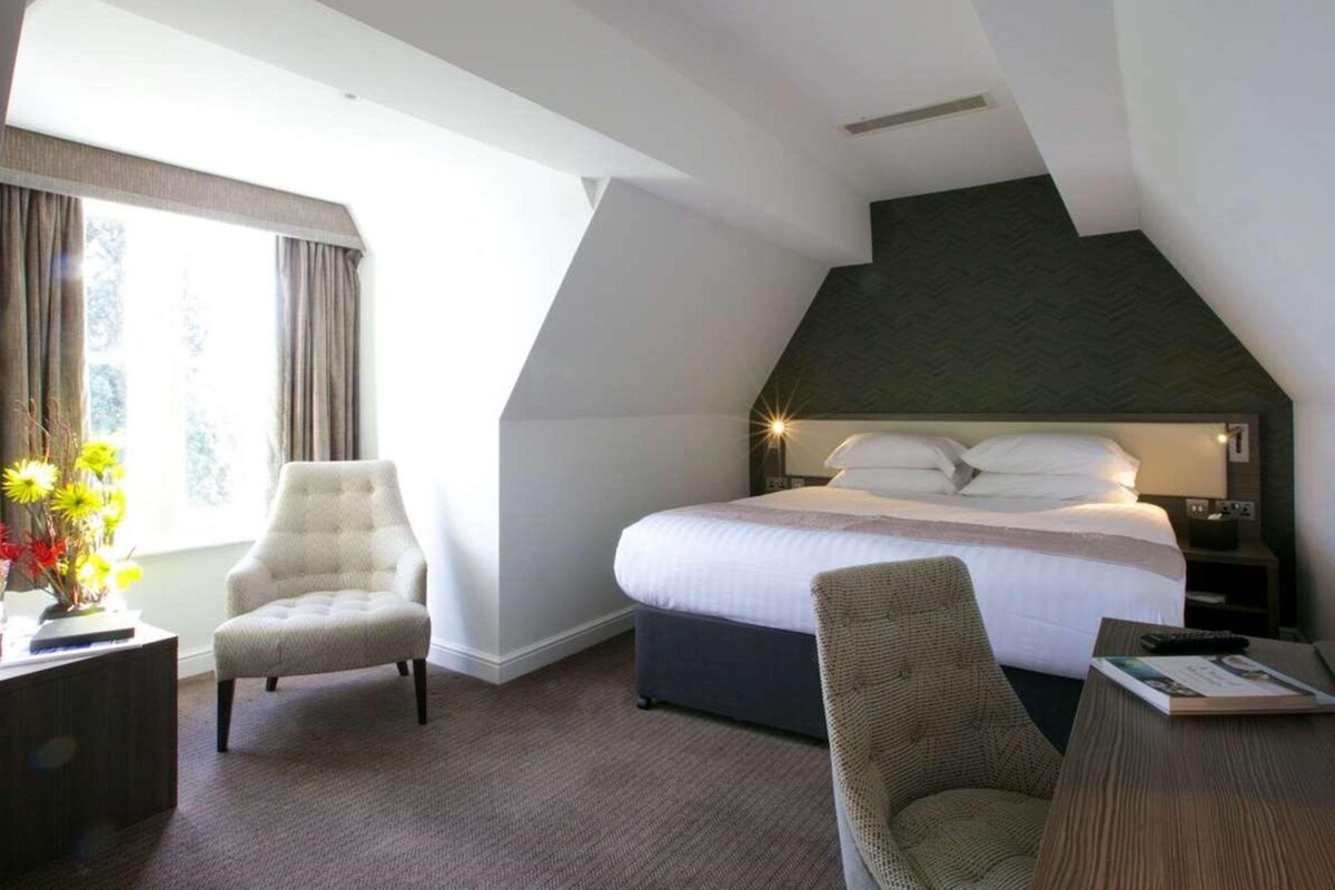 A hotel room with a bed, a chair, a desk, and a window with curtains.