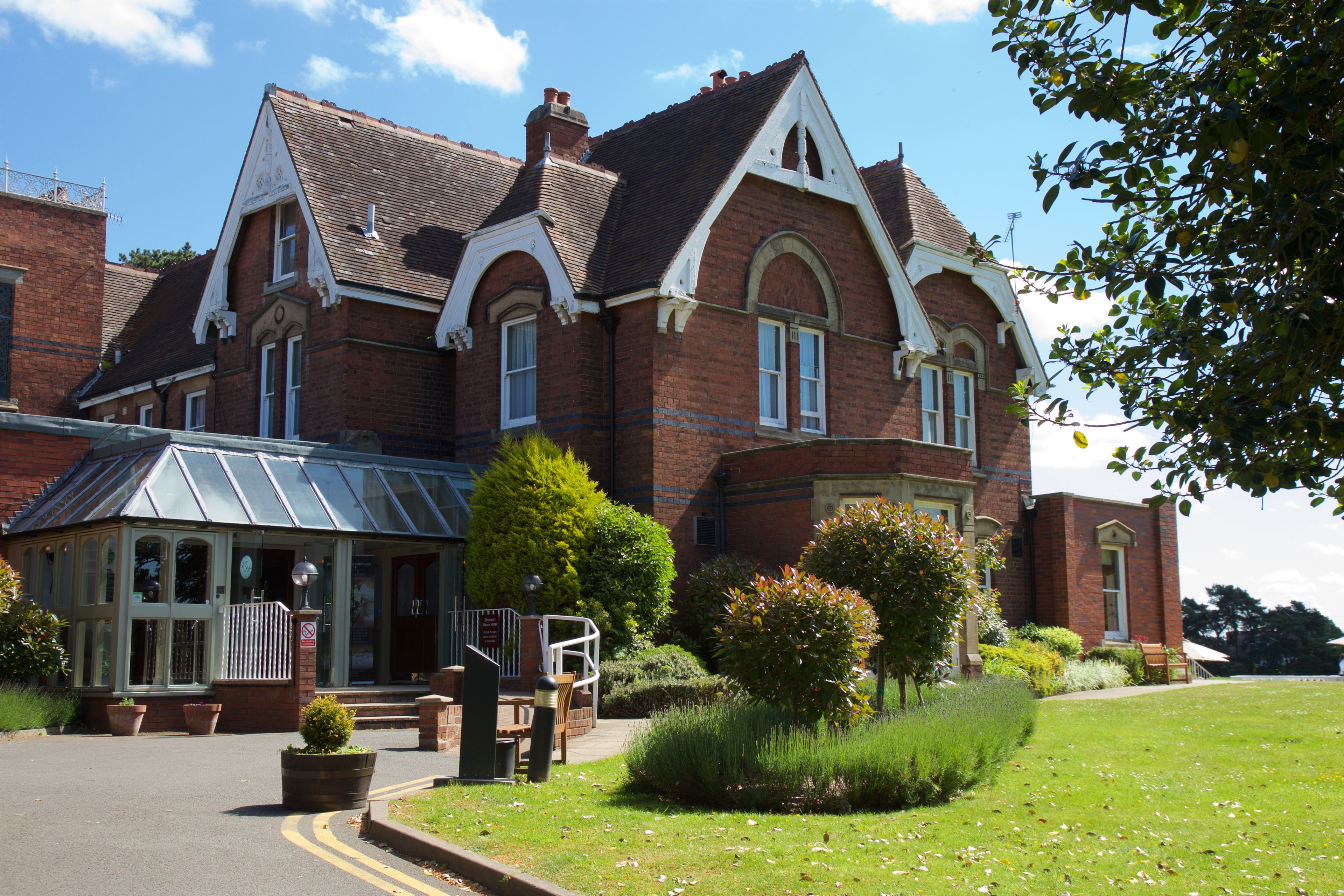 A large, historic building with a prominent entrance, a conservatory, and well-maintained gardens.