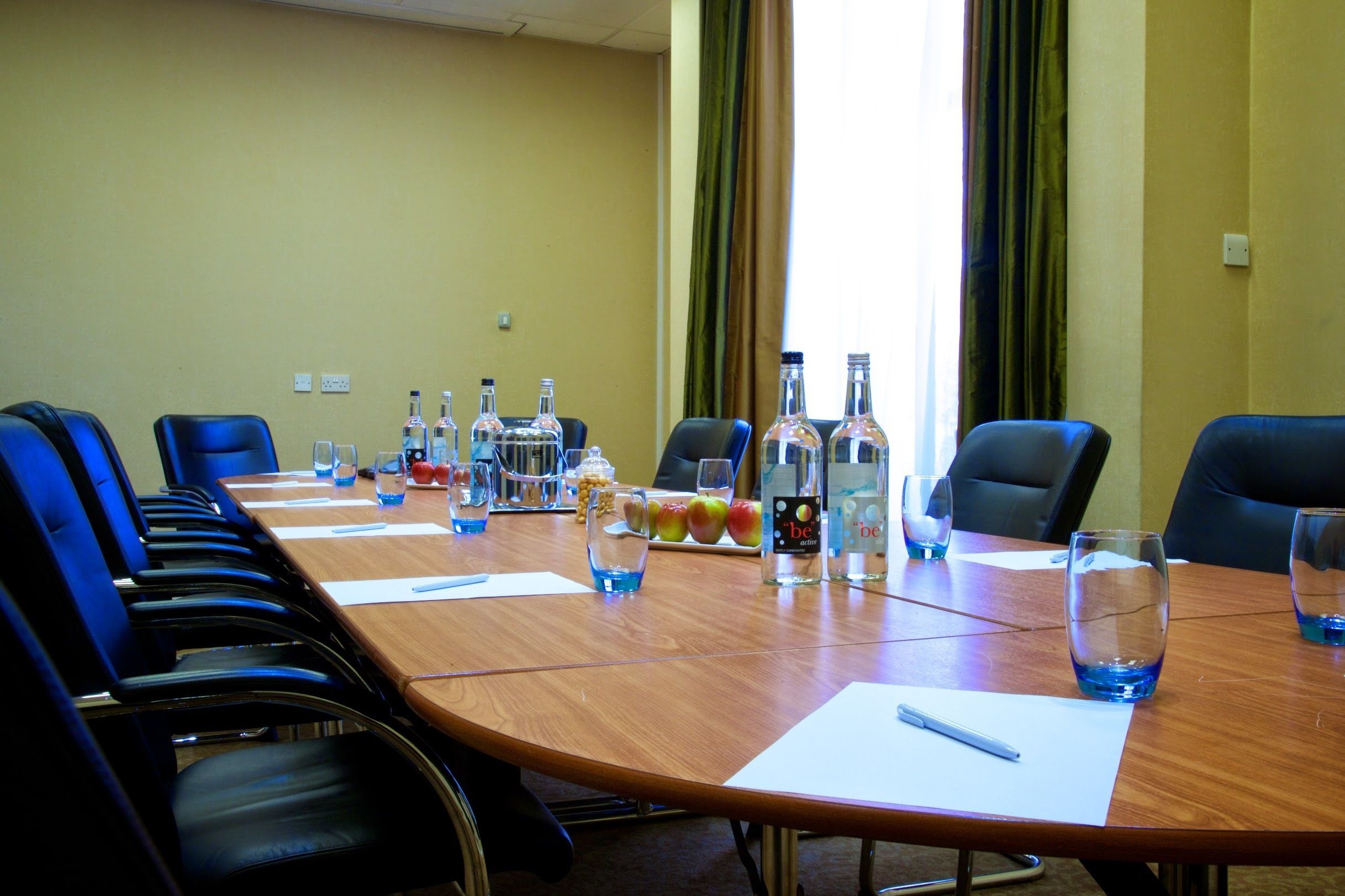 Una sala de conferencias con una larga mesa, sillas y diversos objetos como botellas, vasos y frutas.