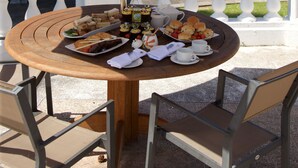 Un área de comedor al aire libre con una mesa redonda, sillas y dos sombrillas grandes.