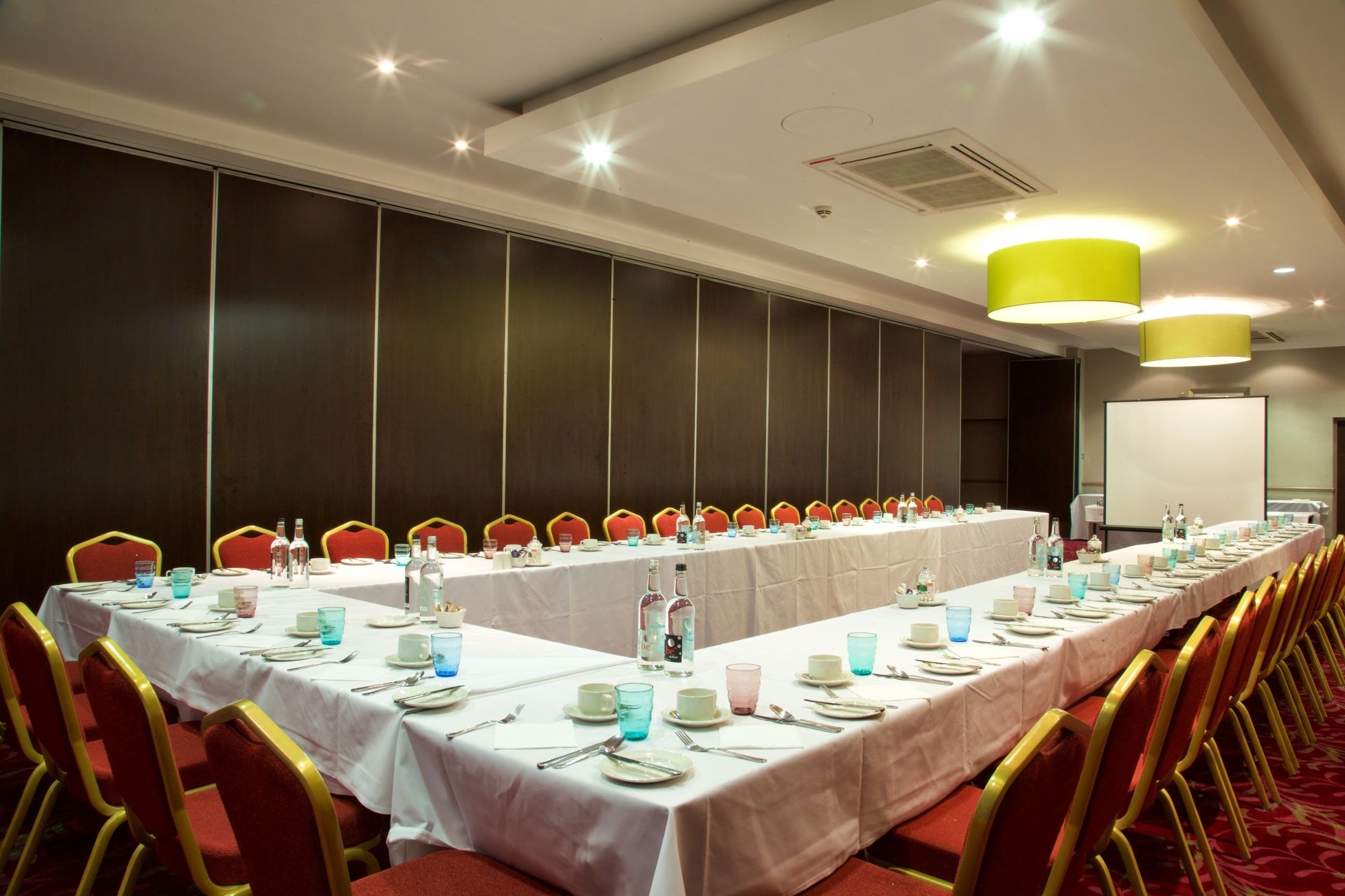 A conference room with a long table set for a meeting, equipped with chairs and tables, and a whiteboard in the background.