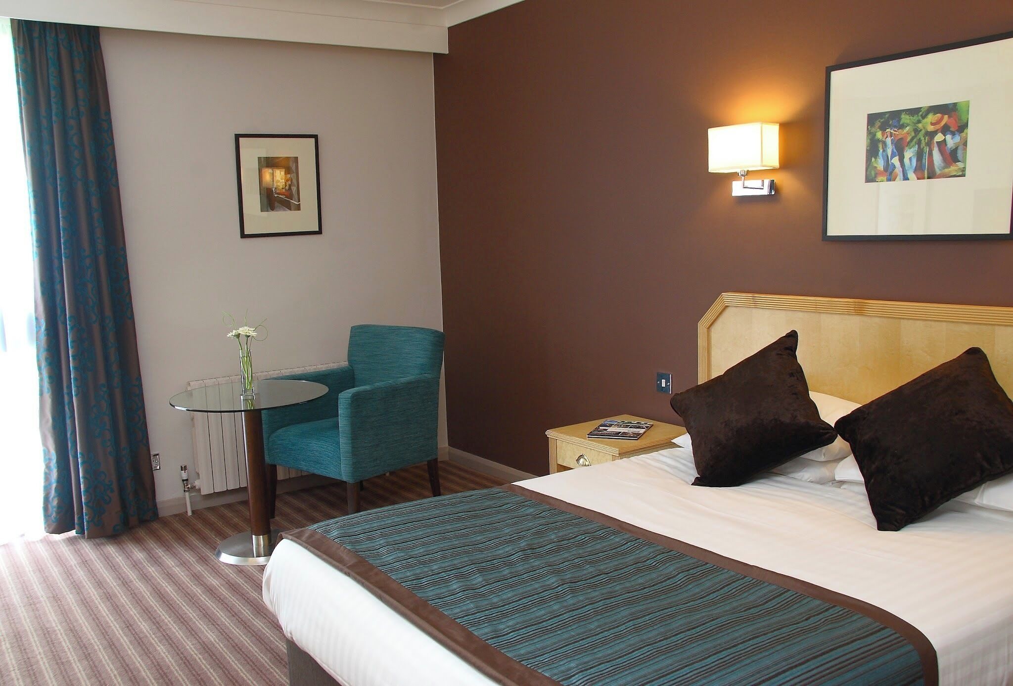 Ein Hotelzimmer mit Bett, Stuhl, Tisch und einem Bild an der Wand.
