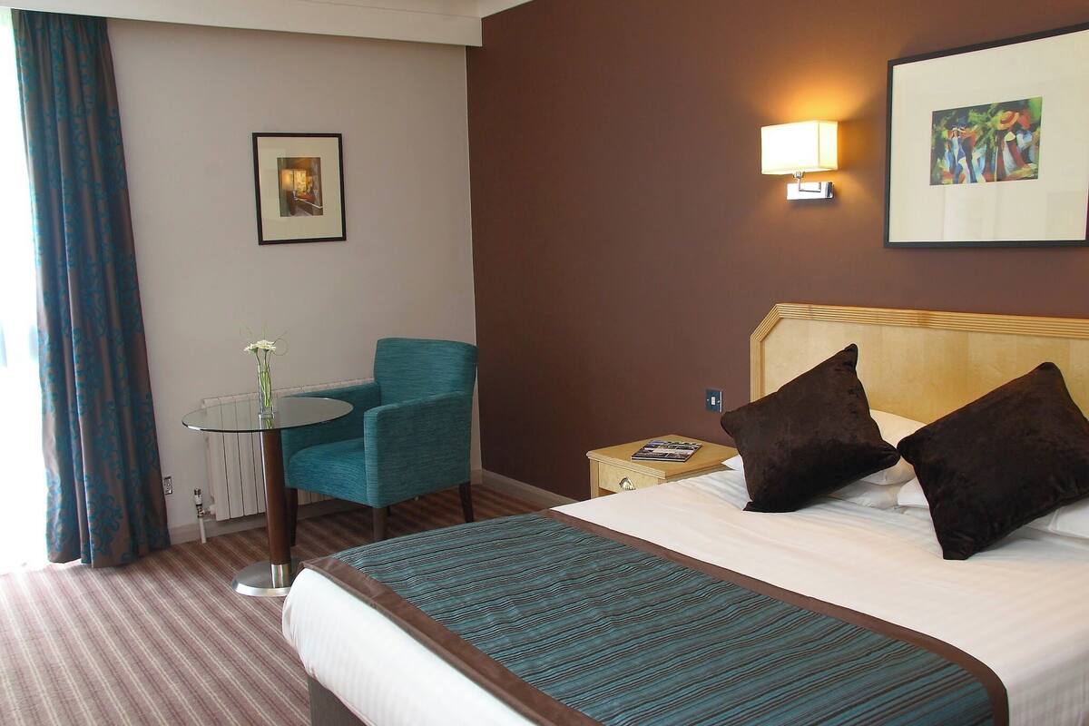 Ein Hotelzimmer mit Bett, Stuhl, Tisch und einem Bild an der Wand.