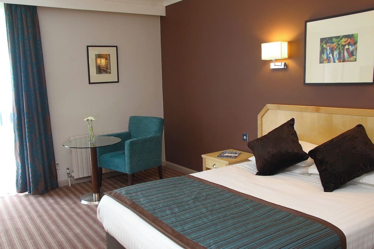 Une chambre d’hôtel avec un lit, une chaise, une table et un tableau au mur.