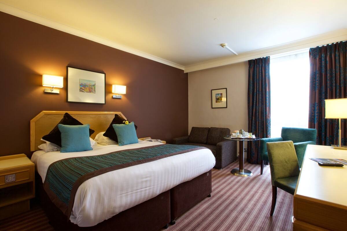 Ein Hotelzimmer mit einem großen Bett, einem Sofa, einem Schreibtisch und zwei Wandleuchten.