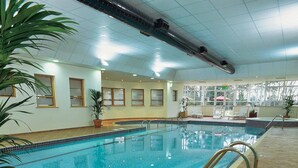 Una piscina interior con agua cristalina y paredes de azulejos, bajo un techo con conductos de aire acondicionado.