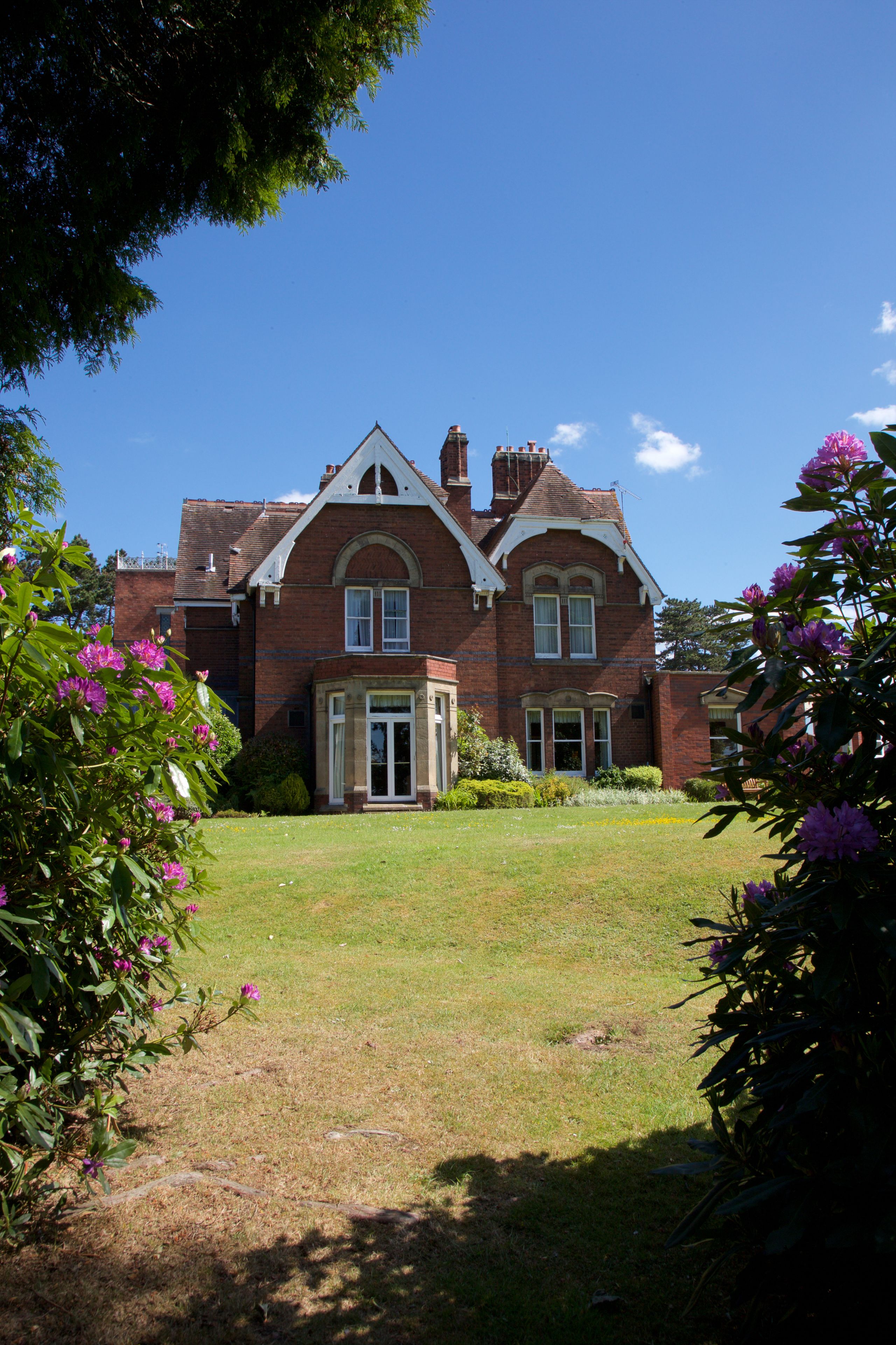 A large brick house with a well-maintained lawn and flowering plants.