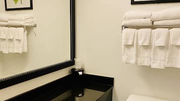 Un baño con encimera negra, lavabo blanco, inodoro e imagen en el pared de hojas enmarco.