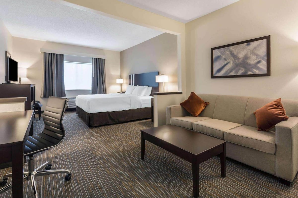 Quarto de hotel com cama, sofá, escrivaninha, cadeira e televisão.