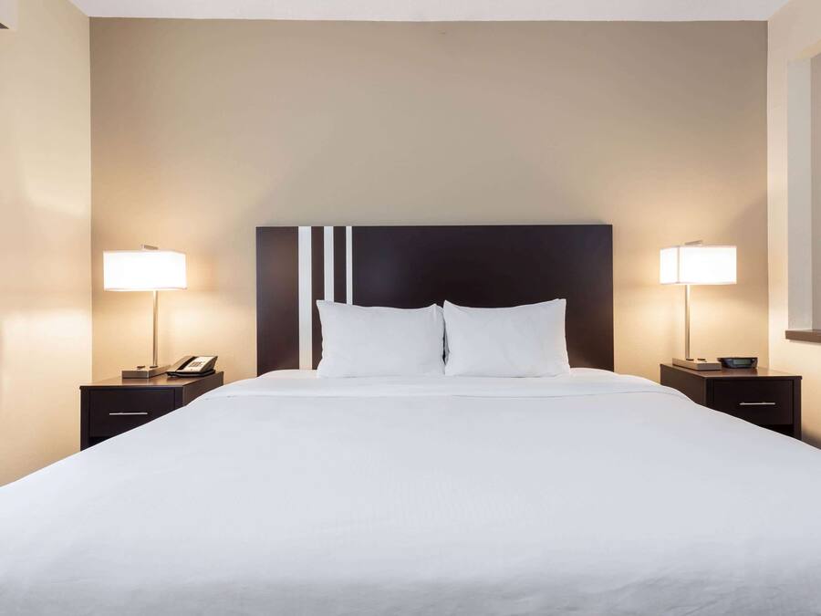 A hotel room with a large bed, two bedside tables with lamps, and a dark headboard.