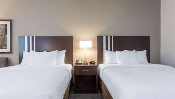 A hotel room with two beds, a nightstand with a lamp, and a framed picture on the wall.