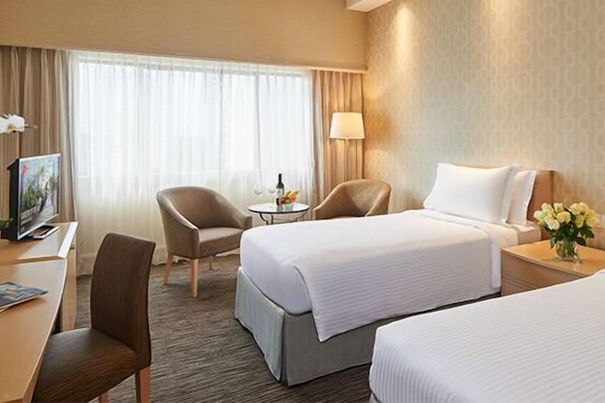 A hotel room with two beds, a desk, a chair, a lamp, and a small table with a vase of flowers.