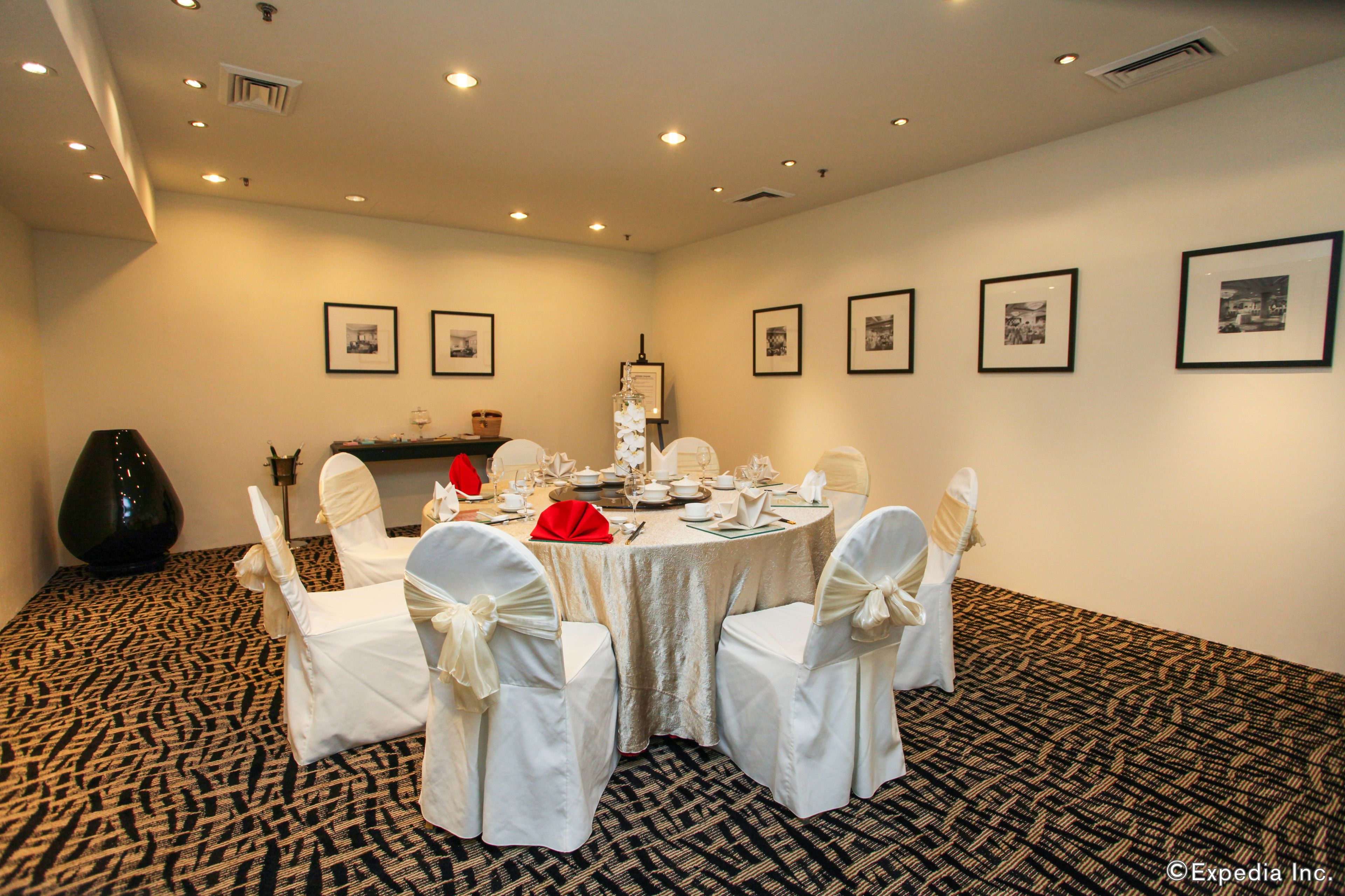 A conference room with a round table, white chairs with bows, and framed pictures on the walls.