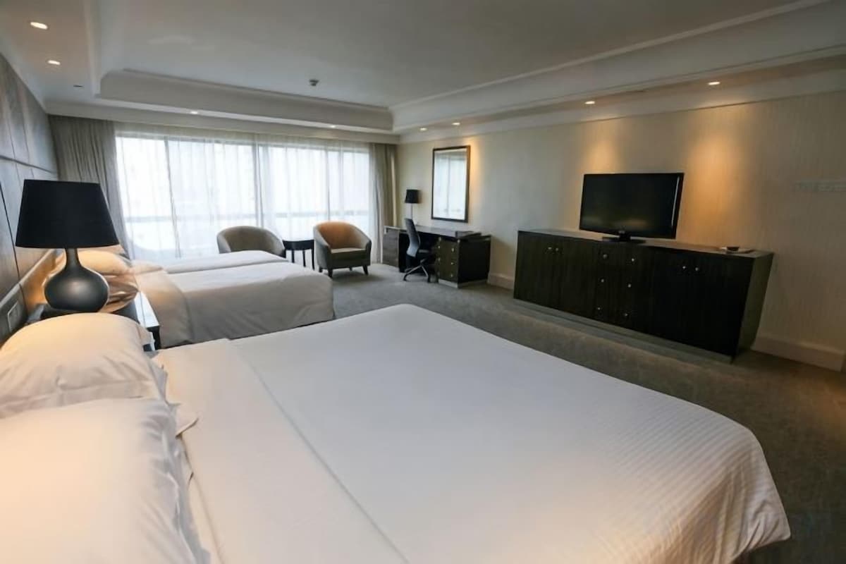 A hotel room with two beds, a desk, a chair, a television, and a large window.
