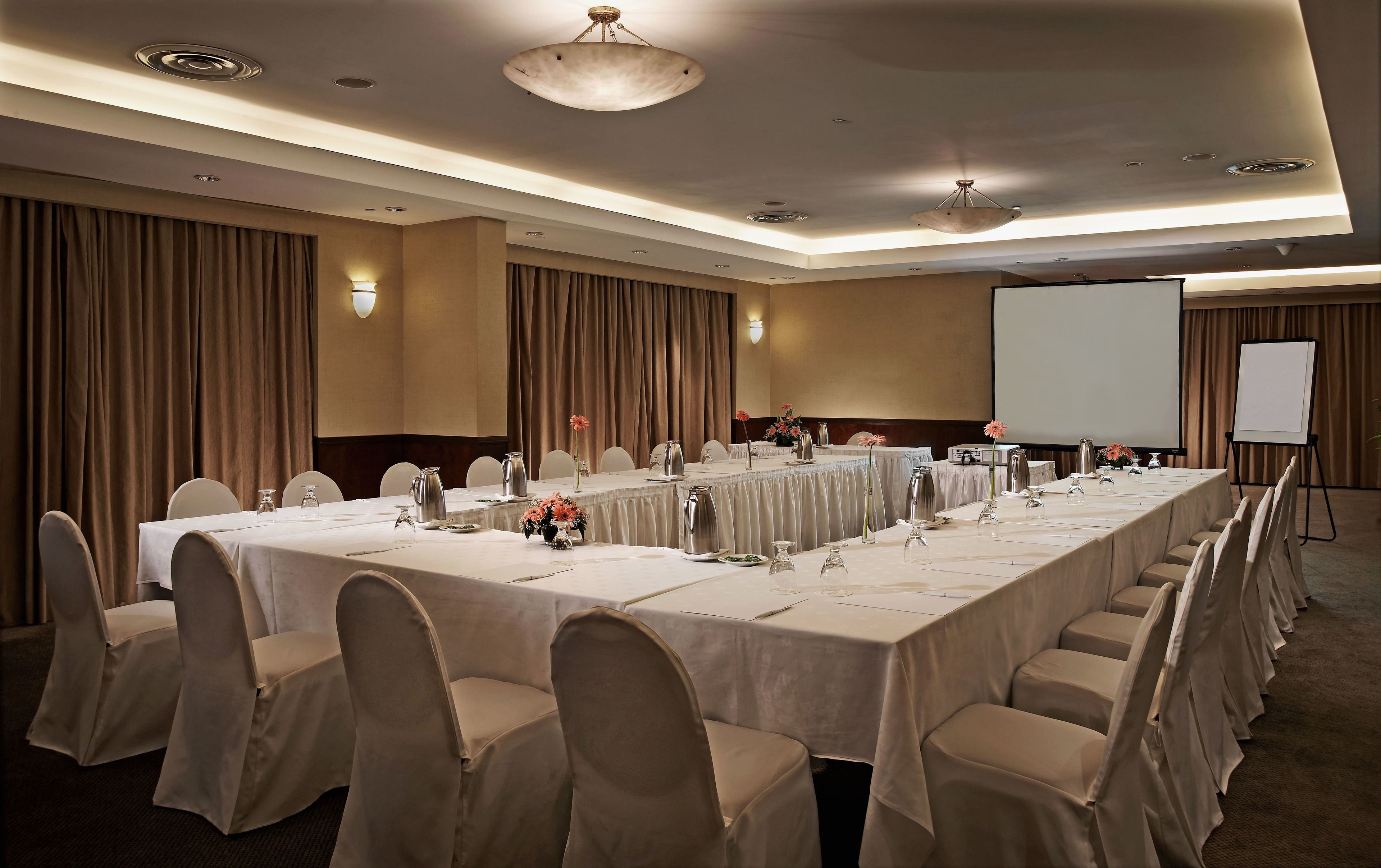A conference room with a long table, chairs, and a projector screen.