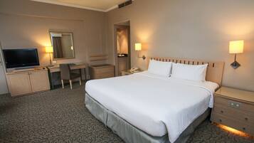 Una habitación de hotel con una cama grande, un escritorio con silla, un televisor y un armario.
